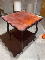 Wood side table with scalloped edges and a lower shelf. Top surface shows wear and scratches. Four curved legs.