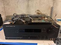 Front view of black Harman Kardon PT2500 receiver with cables and remote on top.