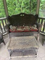 Wicker loveseat with floral cushions on a tiled porch, visible drainage gaps in the wicker with noticeable weathering.