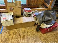Long metal rectangular box, car fender cover, cardboard boxes, and plastic containers on a wooden floor