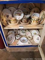 Display cabinet with shelves holding children's plates, cups, pitchers, and bowls with colorful nursery rhyme designs and character illustrations