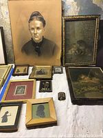 Photo showing 10 pieces of vintage art on a white cloth, including portraits, silhouettes, and prints, arranged flat and leaning against a wall.