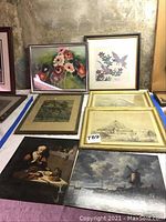 Photo showing all seven framed mixed medium wall art pieces on a surface, arranged to display fronts of paintings and prints with different themes including flowers, birds, landscapes, and buildings.
