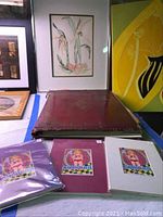 Overall lot view showing framed botanical watercolor painting, worn red leather case, and several matted colorful prints.