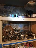 Shelves containing glass candleholders, religious menorahs, and baskets filled with silver plate utensils and serving dishes.