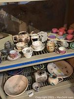 Shelf with metal teapot, ceramic cups and saucers, Raggedy Ann themed metal teapot, colorful plastic tea cups and plates