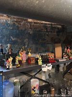 Vintage dolls, figurines, and tin toys arranged on a metal shelf against a stone wall background