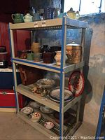 Single gray plastic shelving unit filled with assorted ceramic and glass items including teapots, vases, plates, bowls, and other decorations.