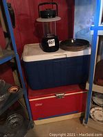 Two coolers stacked: red metal Coleman cooler on bottom, blue plastic Coleman cooler on top; black Energizer lantern on blue cooler lid.