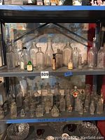 Wide shot of two shelves filled with assorted vintage glass bottles of various sizes and shapes, some labeled, mostly clear glass with some green bottles.