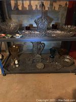 Full view of two shelves filled with assorted vintage cut glass items including bowls, pitchers, and decorative glassware in various shapes and sizes.