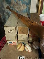 Four cardboard baseball card boxes stacked with a wooden bat resting on top and three baseballs in front