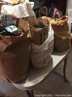 Three large paper bags filled with baseball cards on a table in a basement setting.
