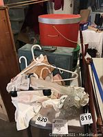 Red round hat box, green rectangular box, cosmetic case and multiple linens hanging on hangers.