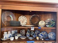 Wide view of plates and serving pieces on wood shelf including Blue Willow, Royal Munich, iridescent platter, and ironstone items