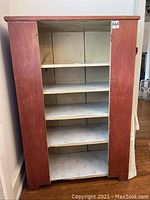 Front view of primitive wooden cupboard cabinet showing red painted sides and open shelves inside.