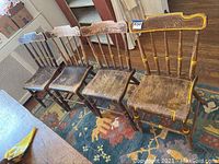 Front view of four primitive wooden chairs showing worn hand-painted details and scratched seats.