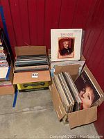 Two cardboard boxes filled with multiple vinyl records showing edges of album covers including Toscanini classical album and another labeled Ultra Soft