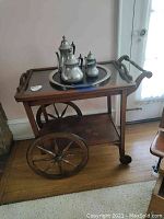 Wooden serving cart with large spoked wheels holding pewter tea set