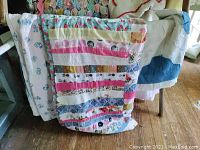 Multi-colored and striped vintage quilts draped over chair showing patchwork and floral designs.