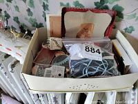 Box containing various small sewing supplies and materials, including tags and small packets, organized together.