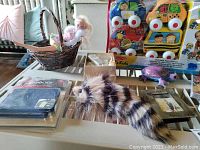 Various small toys on table including Melissa and Doug basket with doll, plush animal, photo frame, gaming accessory, dinosaur toy, armadillo toy, K's Kids vehicles bagged set