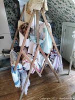 Front-left angled view of vintage wooden quilt rack with quilts draped over tiers. Shows overall design and condition of the rack.