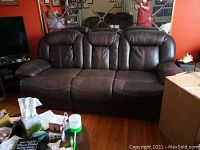 Three-seat brown leather reclining sofa with scratches, showing overall front view and surrounding living room area.