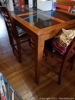 Side view of the wooden pub height dining table showing a glass inlay top and a straight tapered leg. Medium brown finish.