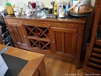 Full front view of wooden server with four cabinet doors and built-in wine rack, various items on top not included.