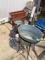 The large aluminum ice bucket on metal stand with several planter boxes in the background, showing outdoor setting.