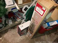 Photo showing boxed 3ft artificial Christmas tree and various boxed decorations and cards on shelves and floor.