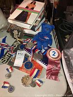 Overview of Howard Stern book stacked with various medals, ribbons, small plush bear, and wooden plaque.