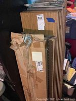 Stack of brown particle board shelving panels with wood grain finish and metal shelf racks wrapped in cardboard.