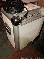 Side and front angled view of ION Block Rocker portable sound system in white metal and aluminum reinforced corners with wired microphone and cable on top.