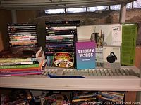 Photo showing assorted books, playing cards, board game '4-Bidden Words', boxed electronic gadget, and a stack of DVDs and Wii games