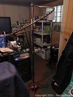 Full view of clothes hanging rack in basement with curved arm and wooden pegs, showing storage area in background