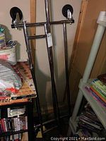 Full view of the folded silver metal dress clothing rack with four wheels, showing the collapsible structure and some scratches on metal.