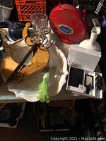 Top view of red quesadilla maker, clear ribbed glass vase, vintage teapot, white decorative vase, ornate metal wall art on wood, multiple trays including white ceramic scalloped and wooden trays, wallet and beauty items in boxes.