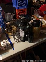 Photo of Alcook juicer with glass carafe, metal napkin holder, and surrounding items on table