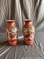 Side-by-side view of two tall ceramic vases with red and white designs featuring birds and floral motifs.