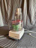 Full view of Cuisinart food processor showing clear plastic bowl, lid, and white base with electrical cord.