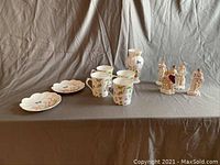 Porcelain assortment on gray background: scalloped-edge plates, three cups, vase, and figurines.
