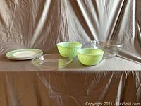 View of all items in the set including plates, green glass bowls, clear glass pie plate, and a large clear glass mixing bowl.