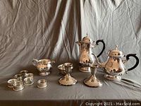 Photo shows the full pewter and plate tea service set including coffee pot, teapot, sugar bowl, creamer, four small cups, two candle holders, and a shallow dish.