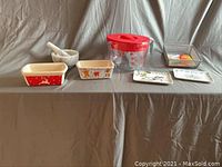 View of all kitchen items arranged on table showing measuring bowl, ceramic dishes, trays, mortar and pestle