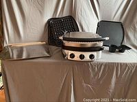 Sharper Image cooking appliance with three interchangeable plates and accessories displayed on a table.