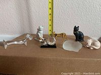 All six figurines placed in a single row on a brown surface against a beige wall with a yellow measuring tape showing height up to 7 inches