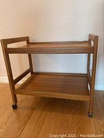 Full view of the two-tier solid wood rolling serving tray or TV stand showing frame and wheels.