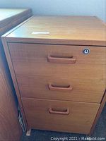 Front view of wooden file cabinet showing three drawers with lock on top drawer.